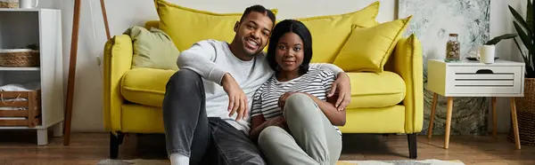 Un couple afro-américain amoureux se détend sur le sol devant un canapé jaune. — Photo de stock