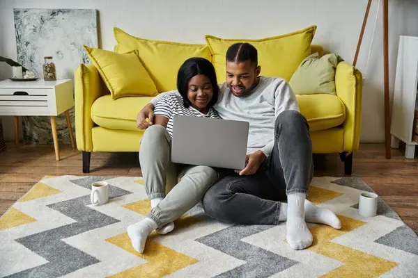 Una coppia afroamericana amorevole si rilassa su un tappeto nel loro salotto, utilizzando un computer portatile. — Foto stock
