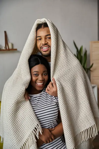 A loving African American couple shares a playful moment under a blanket at home. — Stock Photo