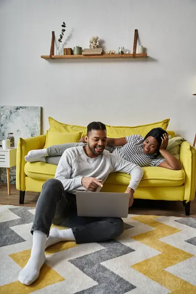 An African American couple relaxes at home on a yellow couch. — Stock Photo