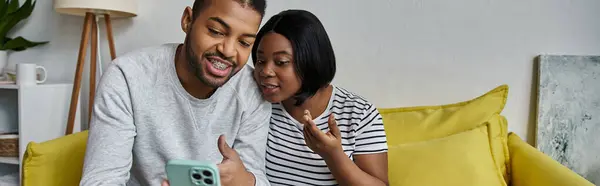 A loving African American couple relaxes on a yellow sofa at home, sharing a laugh together. — Stock Photo