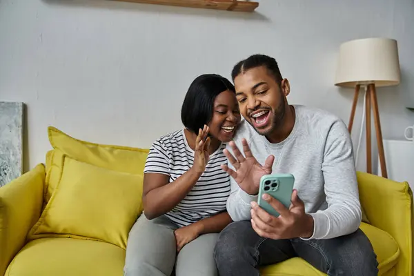 Una coppia afroamericana felice usa il telefono per una video chat mentre si rilassa su un divano. — Foto stock