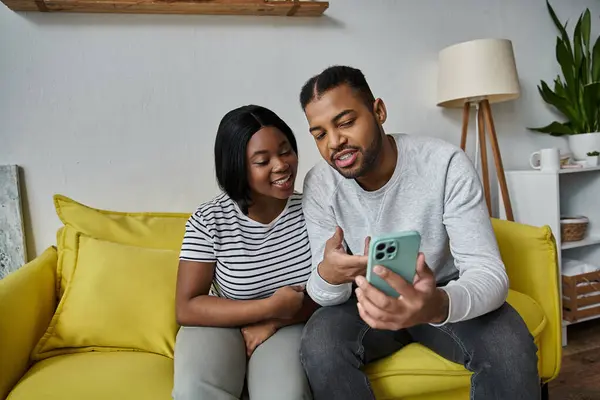 A couple smiles and laughs together while looking at a phone. — Stock Photo