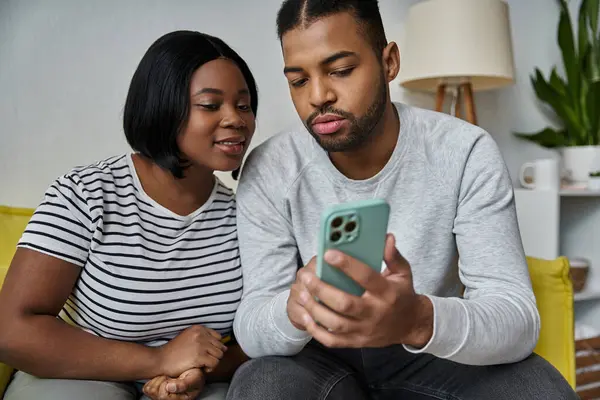 A loving African American couple sits together on a couch, engrossed in their smartphone. — Stock Photo