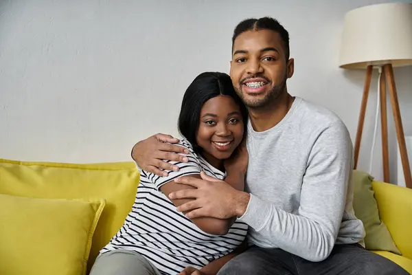 Una coppia afroamericana si siede su un divano, sorridendo e abbracciandosi. — Foto stock