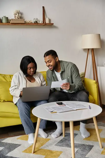 Una coppia afroamericana si siede su un divano giallo, lavorando insieme sulle loro finanze. — Foto stock