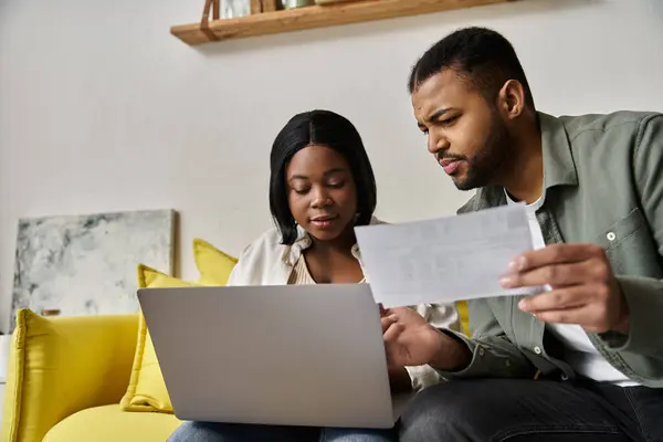 Una coppia amorevole si siede insieme su un divano, recensendo le carte e utilizzando un computer portatile. — Foto stock