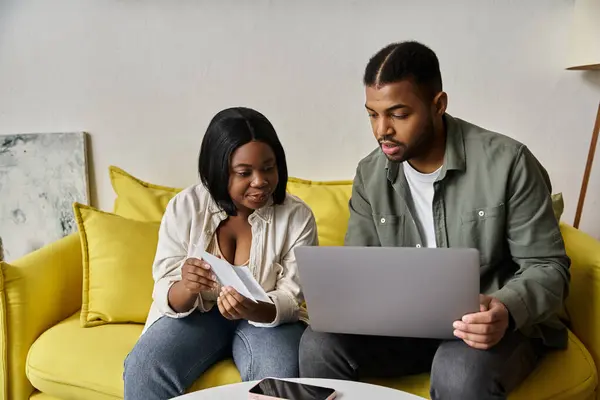 Ein liebevolles afroamerikanisches Paar entspannt sich auf einer gelben Couch und blickt auf einen Laptop. — Stockfoto