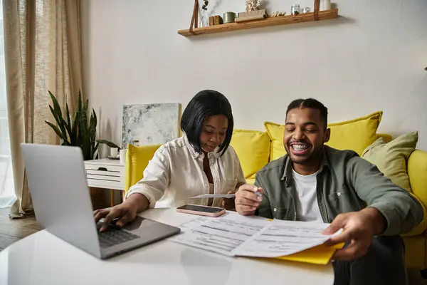 Una coppia afroamericana si siede a un tavolo insieme, guardando documenti e sorridendo. — Foto stock