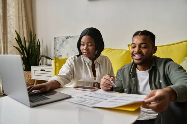 An African American couple sits at a table, reviewing papers and using a laptop. — Stock Photo