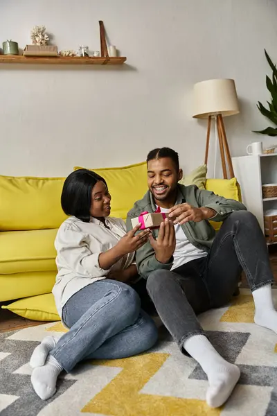 Una coppia felice scambia un regalo su un accogliente pavimento del soggiorno. — Foto stock