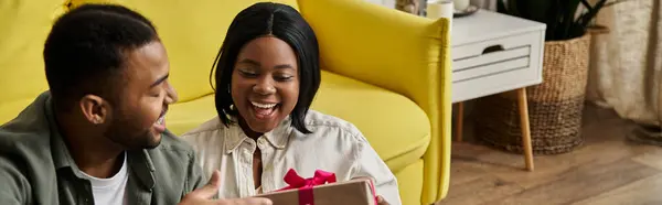 A loving couple shares a happy moment at home, with the woman receiving a gift. — Stock Photo