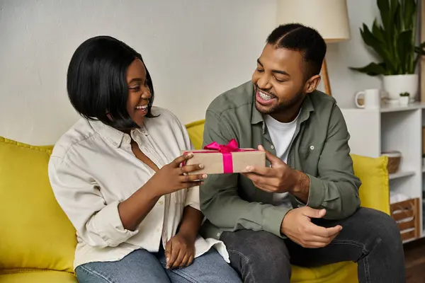An African American couple smiles and exchanges a gift in their living room. — Stock Photo