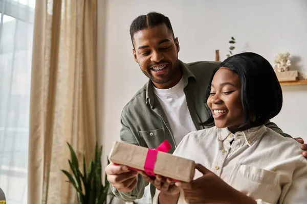 A couple smiles as they exchange a gift at home. — Stock Photo