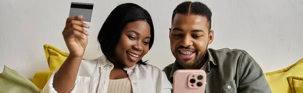 A loving African American couple happily browse online, holding a credit card and a smartphone. — Stock Photo