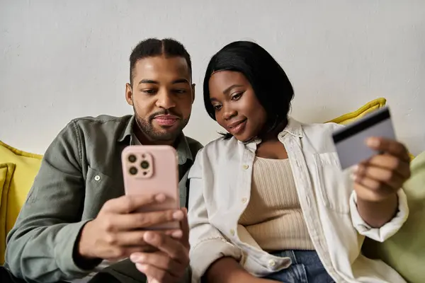 Una coppia di afroamericani acquista online sul loro divano con smartphone e carta di credito. — Foto stock