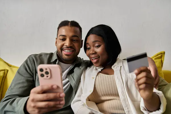 An African American couple smiles at their phone while shopping online at home. — Stock Photo