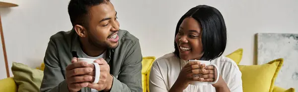 A loving African American couple relaxes on a couch, enjoying coffee and conversation in their home. — Stock Photo
