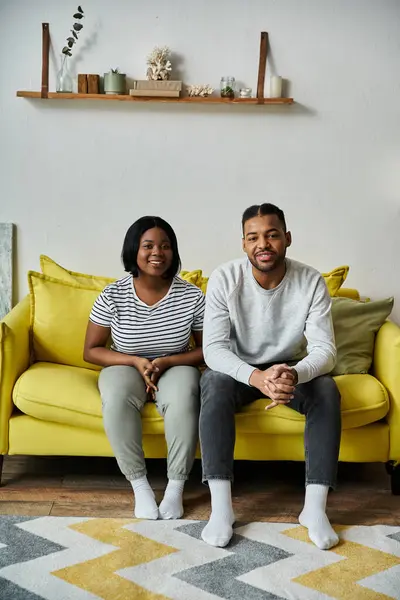 A happy African American couple sits together on a yellow couch in their home. — Stock Photo