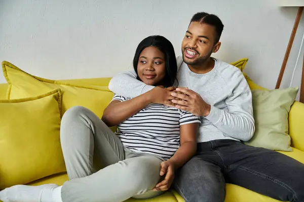 A happy couple cuddles on a yellow couch. — Stock Photo