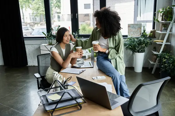 Two women, a lesbian couple, smile and enjoy a coffee break in their office. — Stock Photo