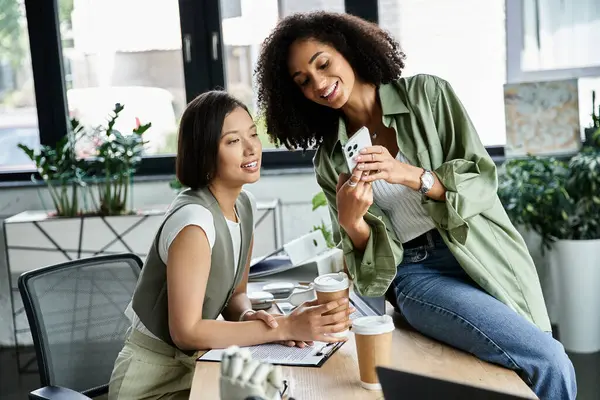 Two women are working together in an office, discussing something on a phone. — Stock Photo