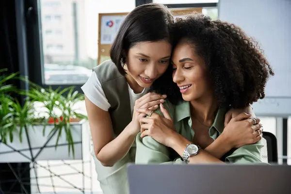 Zwei Frauen arbeiten in einem Büro zusammen, wobei eine Frau die andere liebevoll umarmt. — Stockfoto