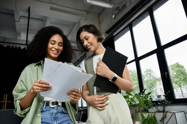 Two women stand in a modern office, reviewing documents together. — Stock Photo