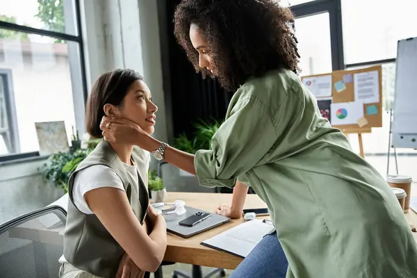 Dos mujeres trabajando juntas en una oficina, con una mujer sosteniendo la mano gentilmente. - foto de stock