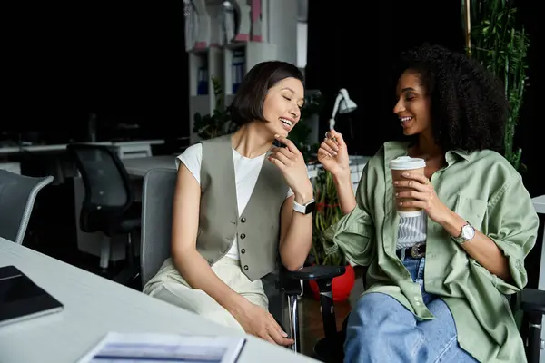 Two women laugh together in an office setting. — Stock Photo