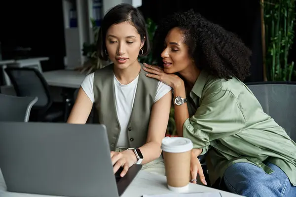 Two women work together in an office, one leaning in to look at the others computer screen. — Stock Photo