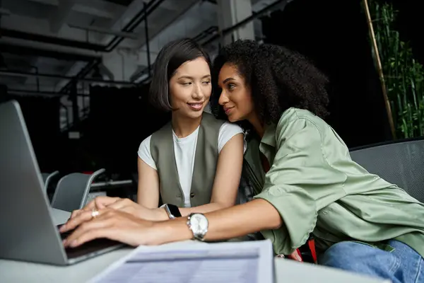 A lesbian couple works together on a laptop in a modern office setting. — Stock Photo