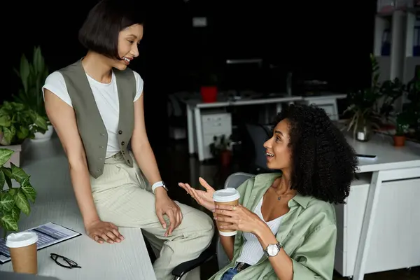 Two women sharing a lighthearted moment over coffee in an office. — Stock Photo