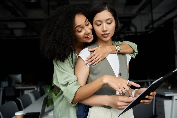 Two women work together in an office, embracing and reviewing documents. — Stock Photo