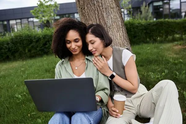 Two women, a lesbian couple, work together on a laptop in a park. — Stock Photo