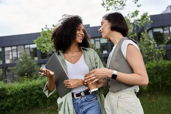 Dos mujeres, aparentemente una pareja, de pie fuera de un edificio, comprometidas en una conversación casual. - foto de stock