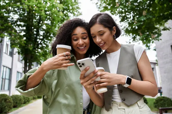 Duas mulheres olham para um smartphone enquanto caminham fora. — Stock Photo