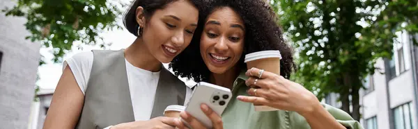 Two women enjoy a coffee break together, laughing while looking at a smartphone. — Stock Photo