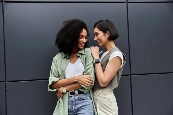 Two women lovingly look at each other while standing in front of a modern urban backdrop. — Stock Photo