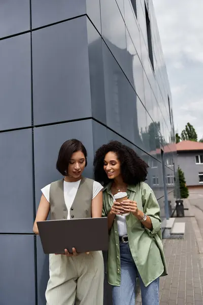 Two women work together on a laptop outside a building. — Stock Photo