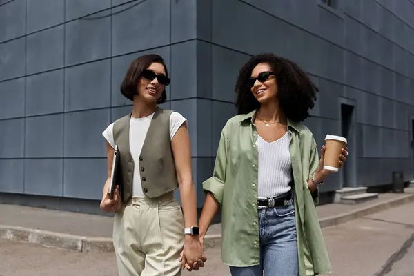 Two women in stylish outfits walk hand-in-hand on a city street. — Stock Photo