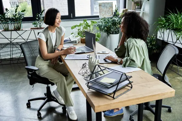 Two women sit at a desk in an office, working together. — Stock Photo