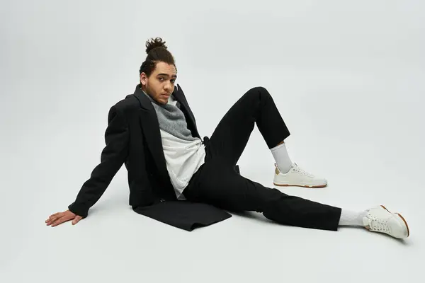 A stylish African American male model wears an elegant coat and sits on a grey background. — Stock Photo
