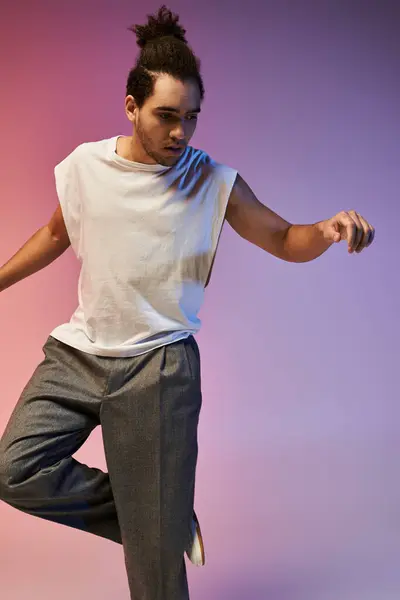 A young African American man dances in a white sleeveless shirt and grey pants against a gradient background of pink, blue, and purple. — Stock Photo