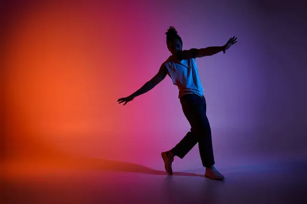 Un jeune Afro-Américain danse avec énergie et grâce sur fond de gradient vibrant. — Photo de stock