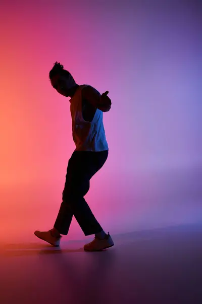 A young African American man dances in a studio, his silhouette framed against a vibrant gradient background of pink and blue. — Stock Photo