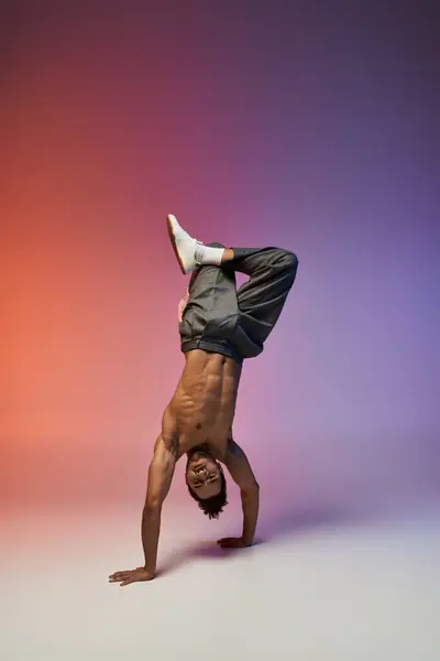 A young African American man performs a handstand against a colorful gradient background. — Stock Photo