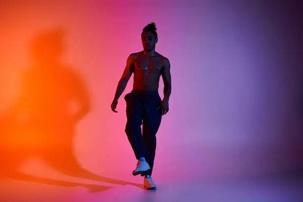 Un jeune Afro-Américain danse sur fond de dégradé rose et orange. Il porte un pantalon noir et des chaussures blanches.. — Photo de stock