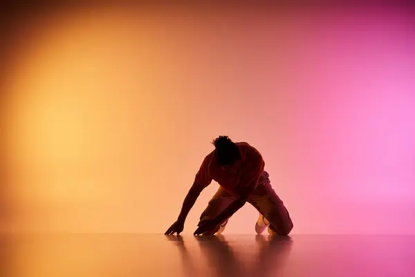Un bailarín afroamericano realiza un movimiento en un estudio con un fondo amarillo y rosa degradado. - foto de stock