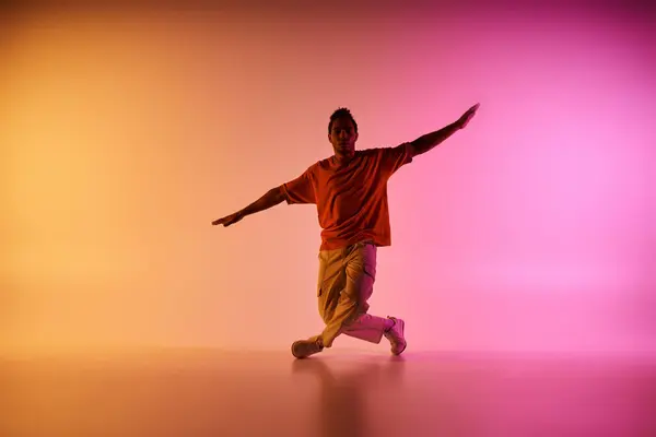 Um jovem afro-americano em uma camisa laranja dança contra um fundo gradiente colorido. — Fotografia de Stock